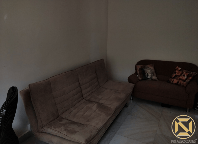Dimly lit waiting area with a tan fold-out sofa and brown two-seater on marble flooring, Hyderabad office