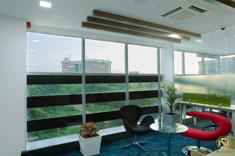 Breakout corner with black Swan chair, red lounge seat, glass table and panoramic city-view windows, Hyderabad