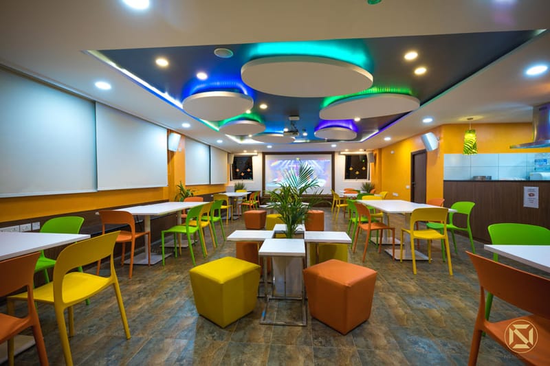 Office cafeteria with colourful chairs, circular LED-lit ceiling coves and orange accent walls, Hyderabad