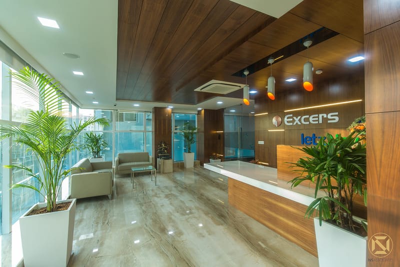 Reception lobby with wood-panelled ceiling, glossy stone floor, leafy potted palms and waiting sofas at Excers Inc, Hyderabad