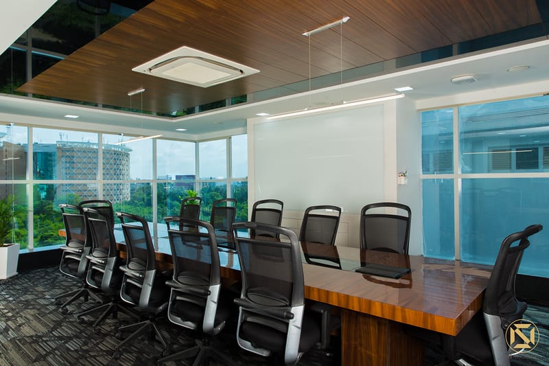 Corner boardroom with polished wood table, black ergonomic chairs and floor-to-ceiling windows over greenery, Hyderabad office
