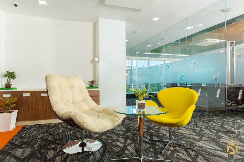 Office lounge with a cream egg chair and yellow swan chair around a glass table beside a frosted glass meeting room, Hyderabad