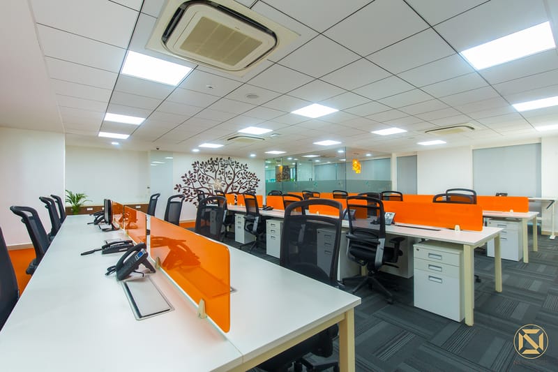 Open-plan office with white desks, orange privacy dividers, mesh chairs and a tree wall decal under a grid ceiling, Hyderabad
