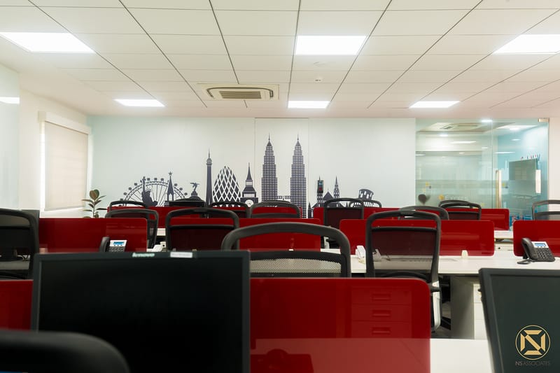 Open-plan office workstations with red desk partitions and a black city-skyline wall decal under recessed lighting, Hyderabad