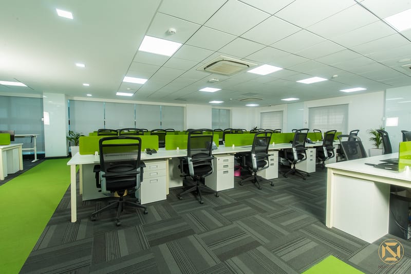 Open-plan office with white desks, lime-green privacy screens, black mesh chairs and grey carpet tiles, Hyderabad workspace