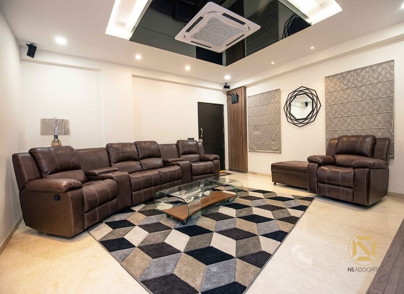 Spacious living room in Hyderabad with brown leather reclining sectional, 3D-cube area rug and textured wall panels framing a round mirror