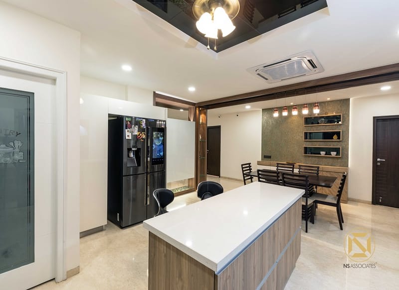 Open kitchen and dining in Hyderabad with white waterfall island, black fridge, breakfast bar stools and ceiling cassette AC