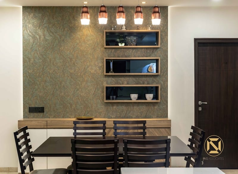 Dining nook in Hyderabad with textured green-and-copper accent wall, glass-front display niches, copper pendant lights and dark chairs