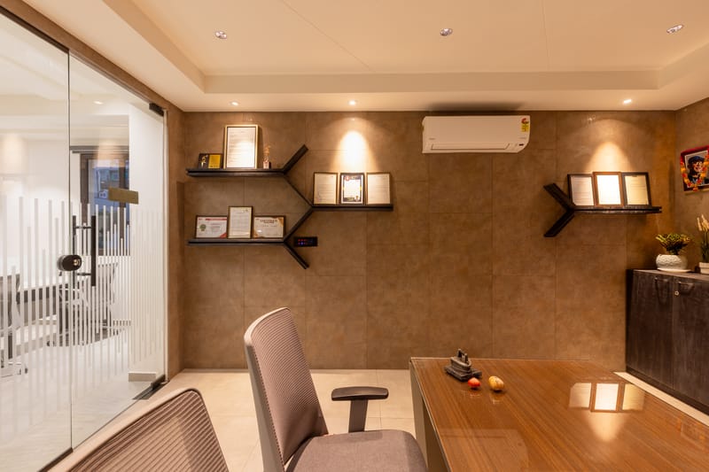 Private office cabin with wooden desk, grey leather chair, framed certificates on a textured tan wall and recessed lighting, Hyderabad