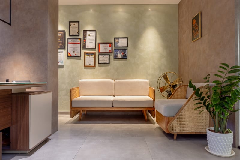 Office waiting nook with cushioned wood-frame sofa, cane bench, framed certificate wall and potted plant, Hyderabad