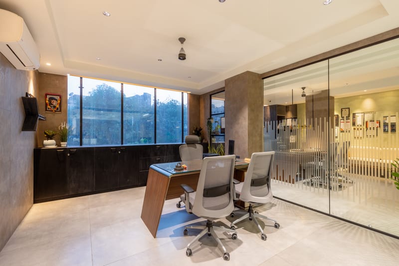 Manager cabin with walnut desk, dark cabinetry, grey chairs and a wide window beside a fluted glass screen, Hyderabad
