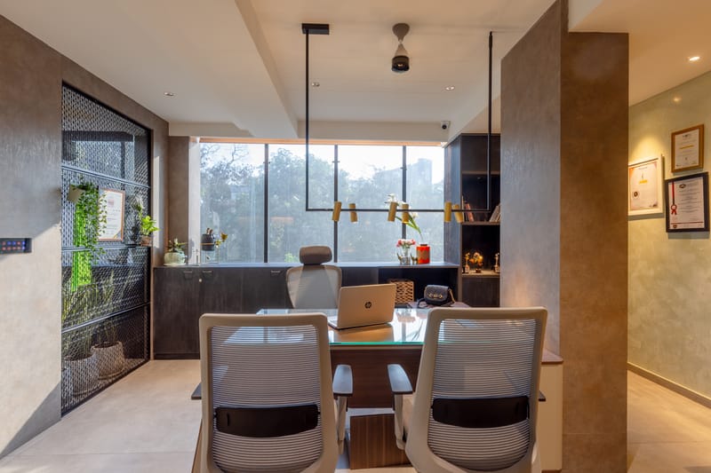 Private office cabin with glass-top desk, mesh-screen planter wall, dark joinery and a greenery-filled window, Hyderabad
