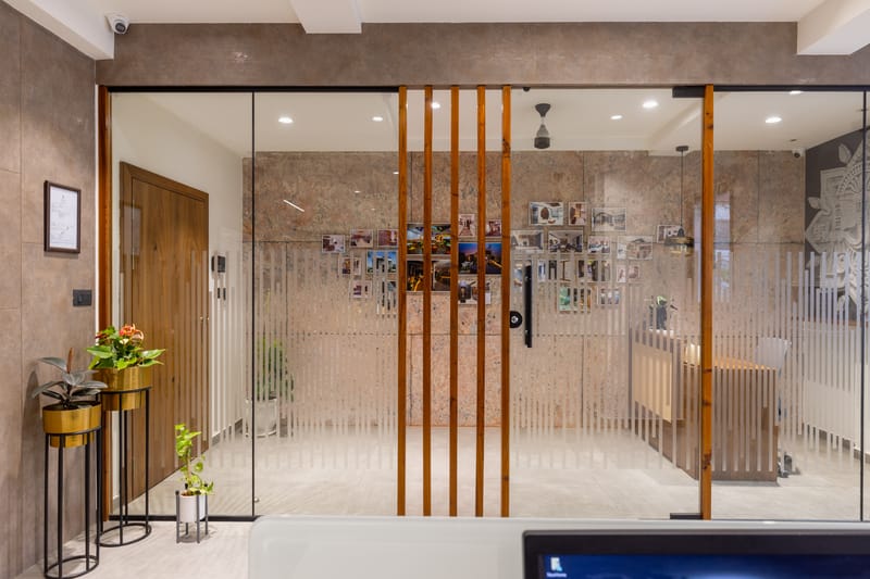 Office entryway framed by fluted glass partition with vertical wood mullions, plant console and photo wall beyond, Hyderabad