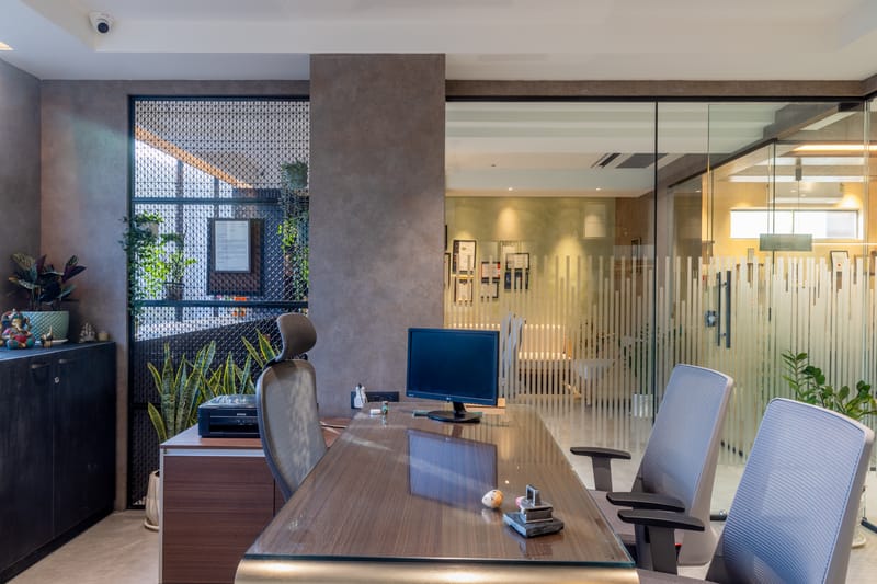 Office cabin with wood desk, perforated metal planter screen, fluted glass partition and grey visitor chairs, Hyderabad