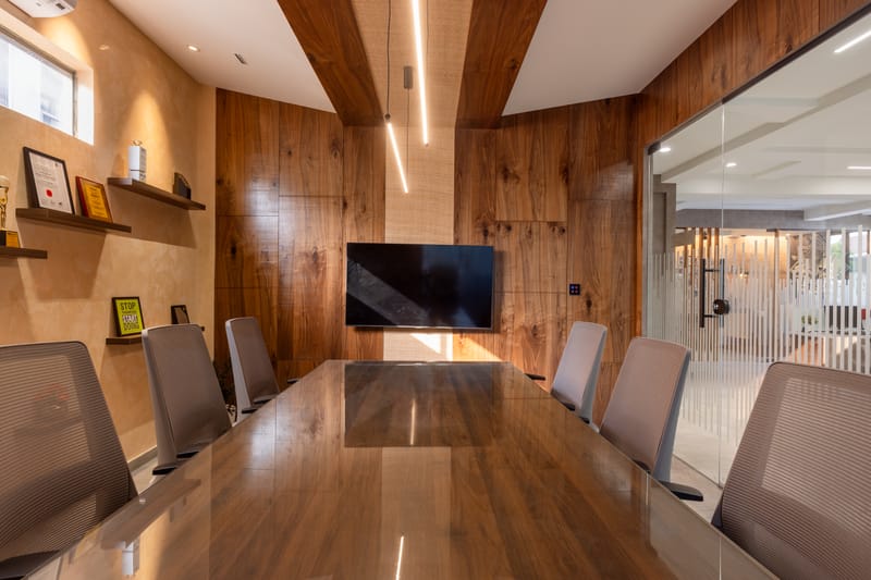Walnut-panelled boardroom with glossy timber table, mesh chairs, wall TV, linear LED and fluted glass wall, Hyderabad