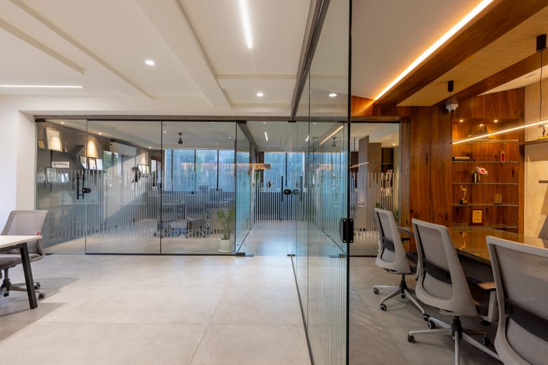 Glass-partitioned office cabin with fluted glass screen, wood-clad wall, LED-lit shelving and grey task chairs, Hyderabad