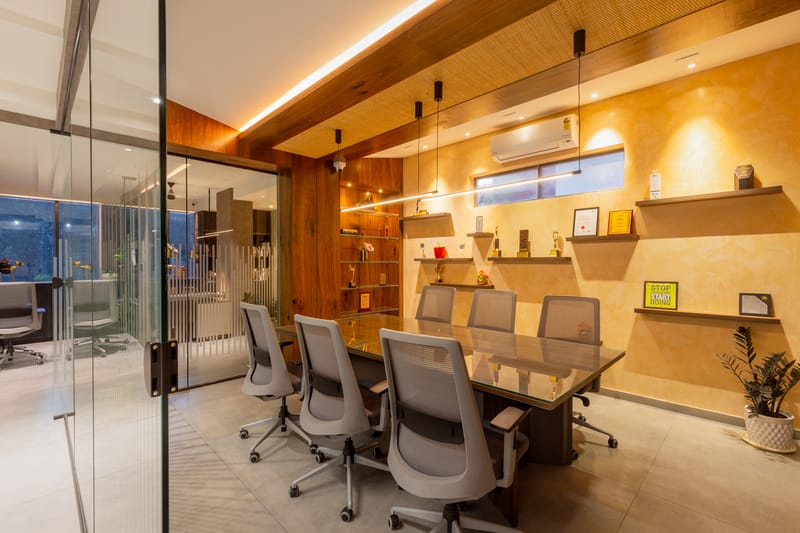 Conference room with textured ochre wall, wood-clad cove-lit ceiling, glass meeting table and grey chairs, Hyderabad