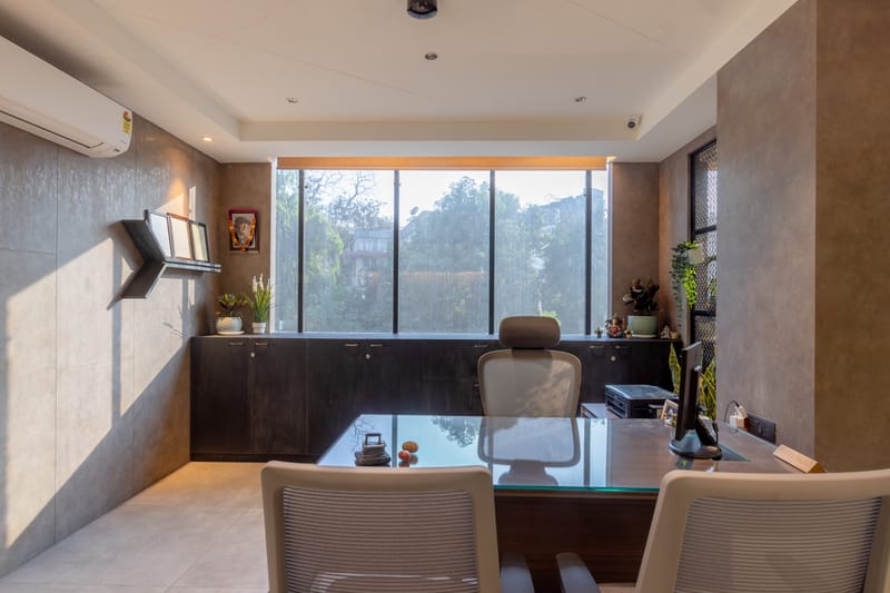 Director's cabin with glass-top desk, brown textured walls, dark credenza and a wide window overlooking greenery, Hyderabad
