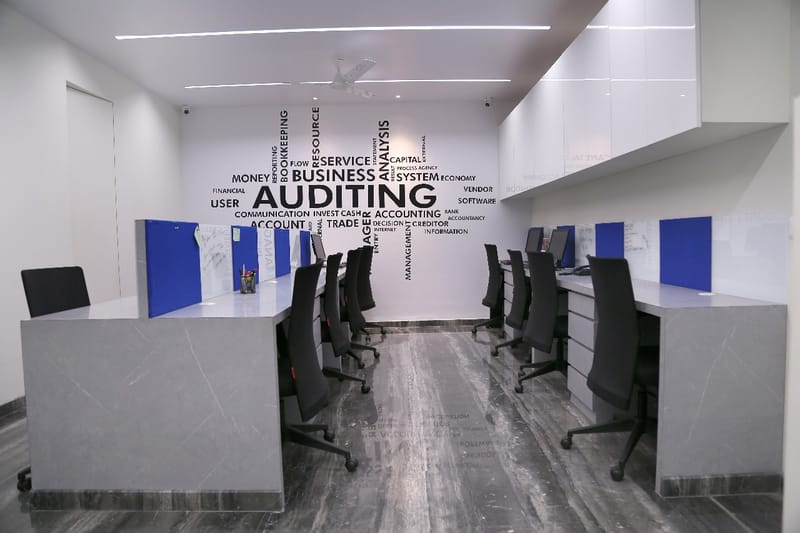 Grey-marble workstation pods with blue dividers below a bold Auditing typography wall, Hyderabad office