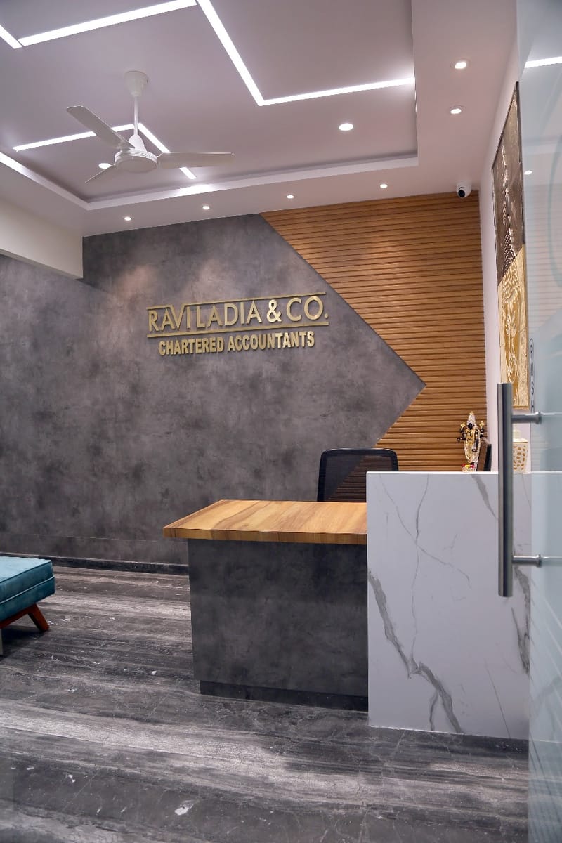 Reception with gold Ravi Ladia & Co signage on grey textured wall, wood-slat panel and marble desk, Hyderabad