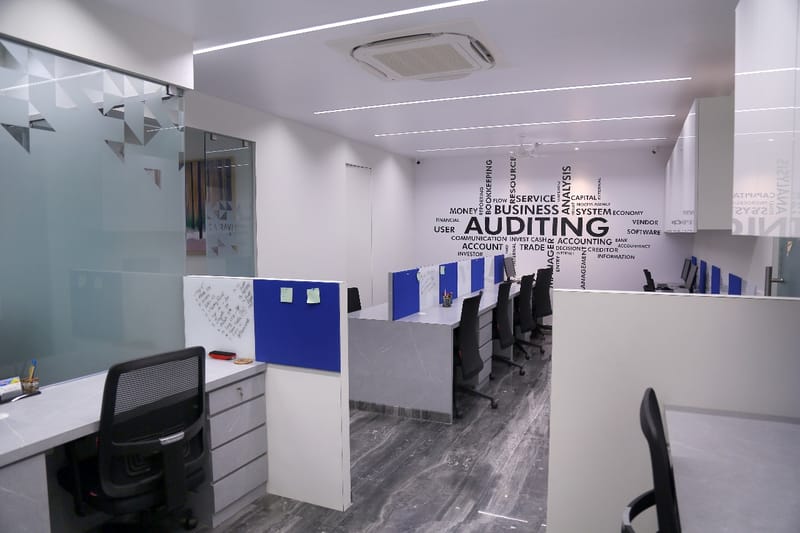 Open-plan workstation bay with blue-screen partitions and an 'Auditing' word-cloud wall graphic, Hyderabad