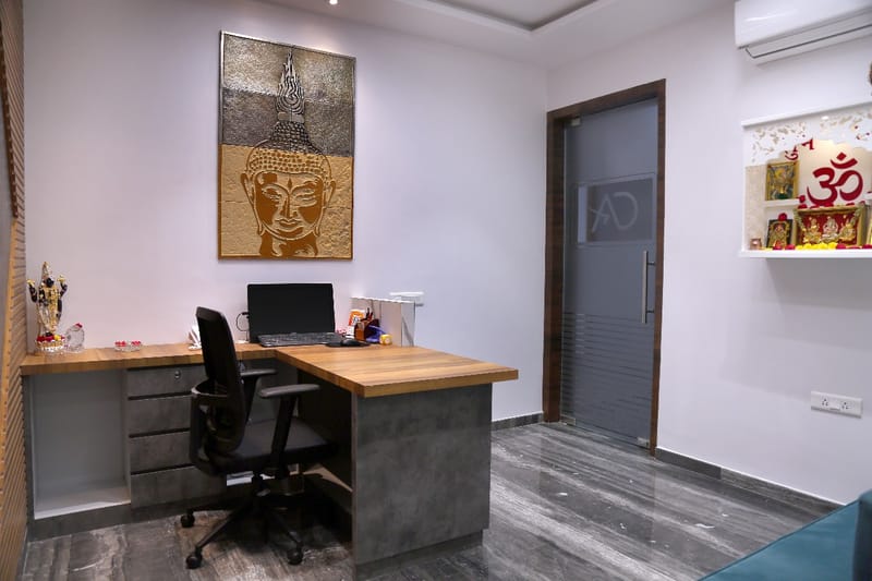 Workspace with wood-and-concrete L-desk, gold Buddha artwork and a small pooja niche, Hyderabad office