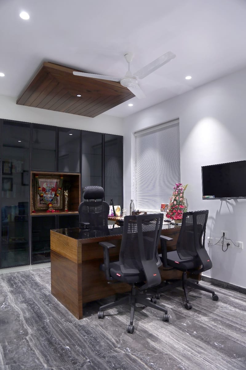 Director cabin with wood ceiling raft, glass-front storage, gold deity frame and twin mesh chairs, Hyderabad
