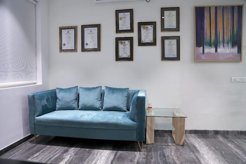 Office waiting lounge with teal velvet sofa, framed certificates and a forest-toned painting in Hyderabad