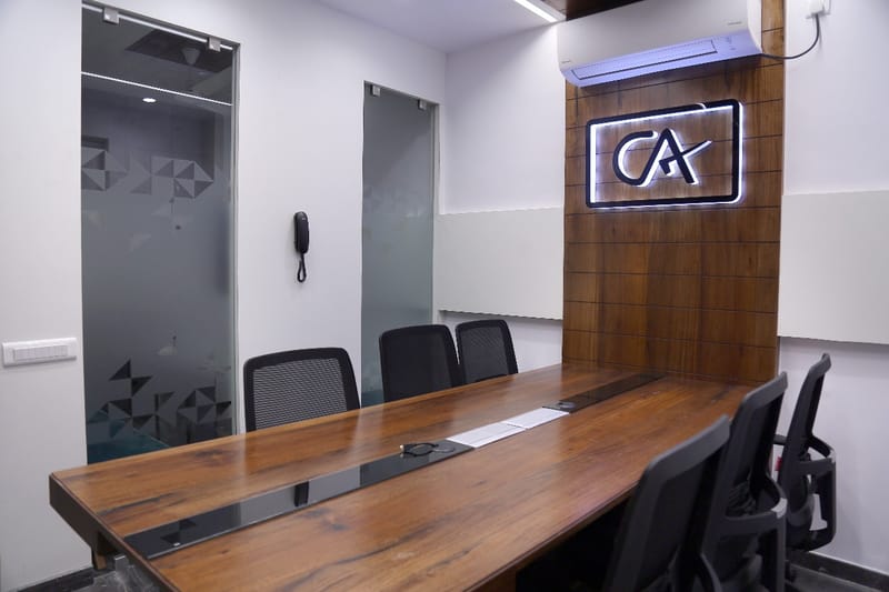 Conference room with long walnut table, mesh chairs and a backlit CA logo on a wood feature wall, Hyderabad