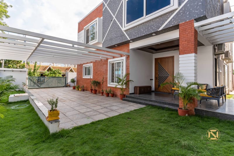 Villa exterior with red-brick and grey stone facade, pergola-covered patio and lawn leading to a wood front door, Hyderabad