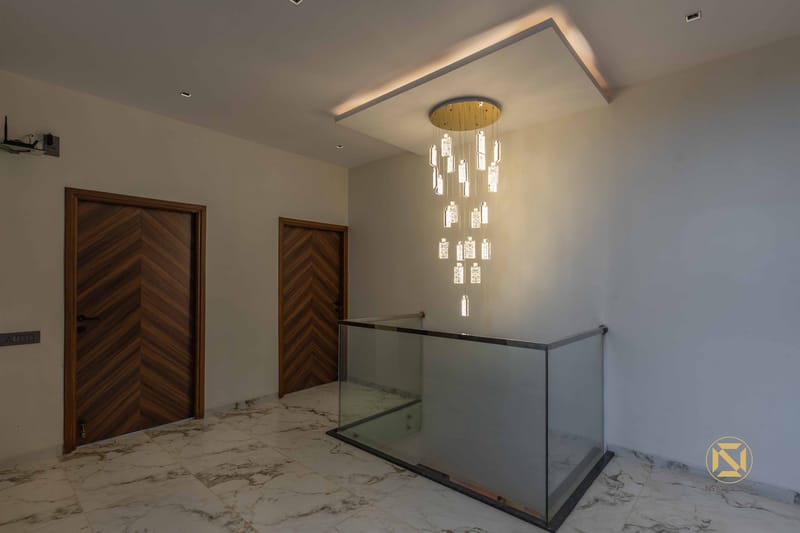 Stair landing with cascading crystal pendant chandelier, walnut chevron doors and glass railing over marble floor, Hyderabad
