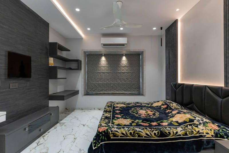 Charcoal-toned bedroom with TV wall, textured backlit niche, floral bedspread and black tufted bed, Hyderabad