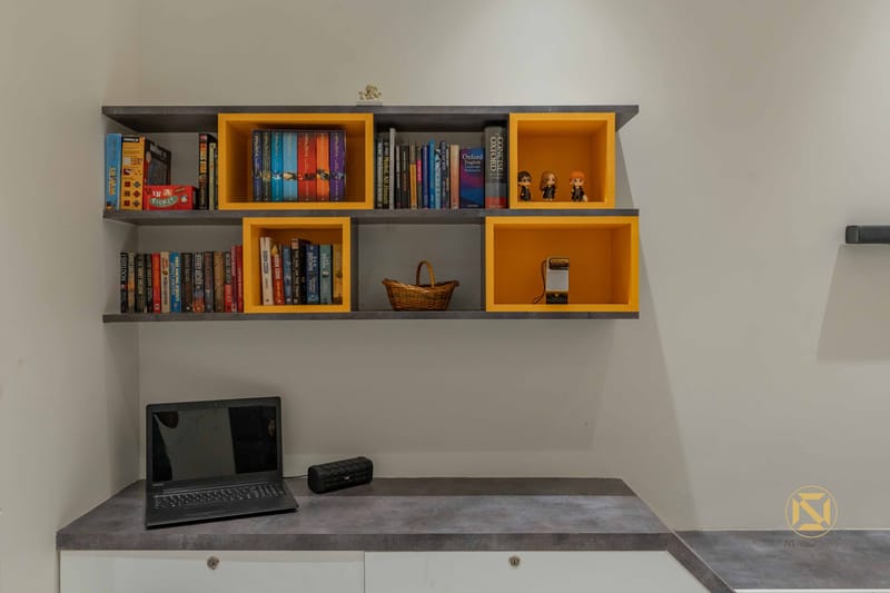 Study nook with floating grey shelves and bright yellow display cubes holding books, above a laptop on a stone-top desk, Hyderabad