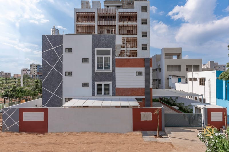 Exterior rear facade of a Hyderabad residence with textured grey tile, red accent band and white louvre detailing