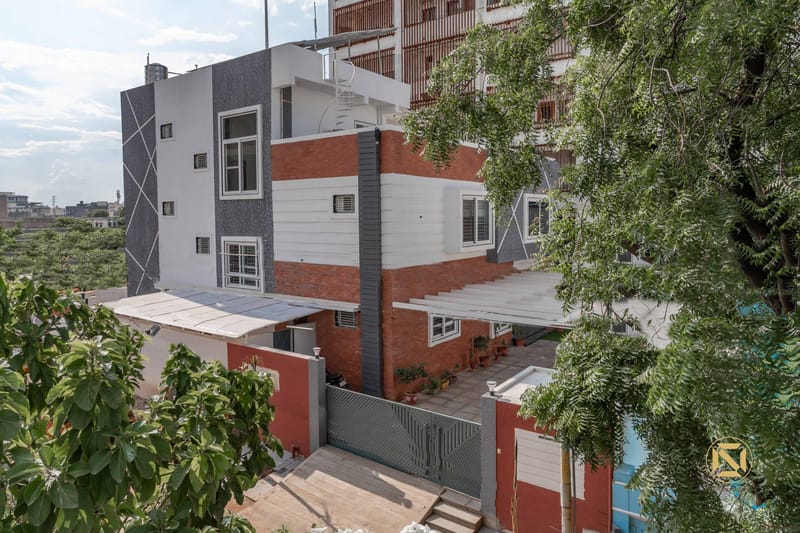 Three-storey Hyderabad home exterior with brick and grey-tile facade, stepped roofline and surrounding greenery