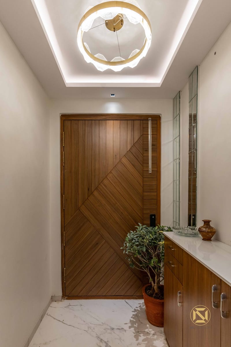 Entrance foyer with chevron-pattern teak wood door, ring chandelier in a cove ceiling and marble flooring, Hyderabad