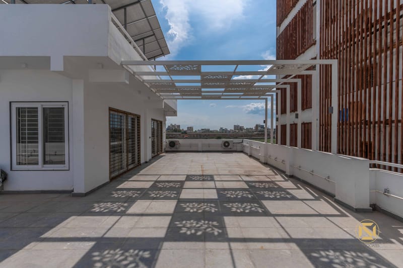 Rooftop terrace with white pergola casting floral shadow patterns on tiled floor, city skyline beyond, Hyderabad