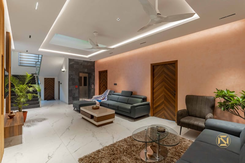 Open living room with peach textured wall, grey leather sofas, glass coffee table and staircase beyond, Hyderabad