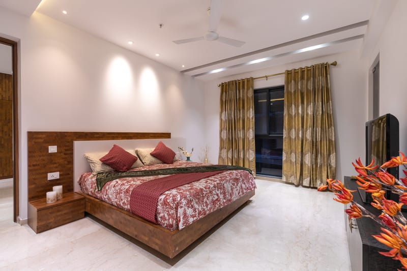 Spacious bedroom with timber platform bed, gold patterned curtains, recessed lighting and marble floor, Hyderabad