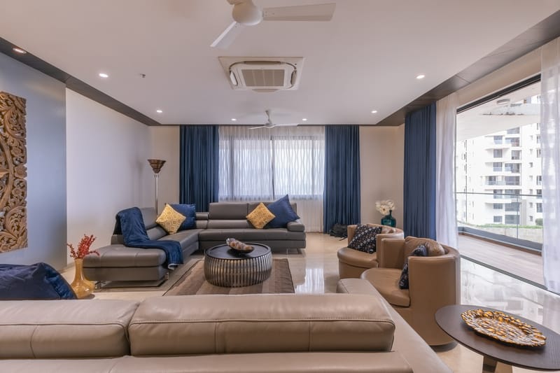 Living room with tan leather sofas, navy curtains, round coffee table and balcony view, Hyderabad apartment