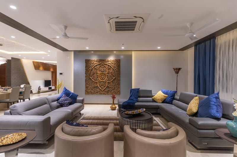 Spacious living room with grey leather sectionals, blue and yellow cushions, mandala wood panel and marble flooring, Hyderabad