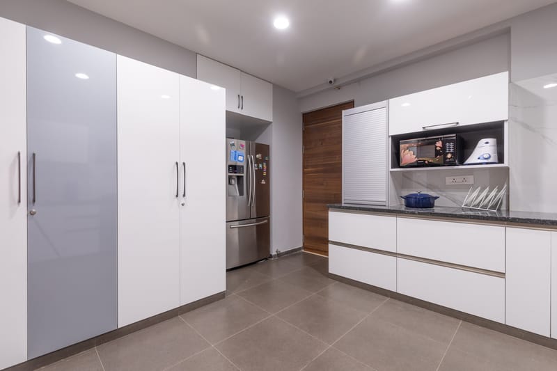 Modern kitchen with tall white and grey gloss cabinets, stainless steel fridge, marble backsplash and granite counter, Hyderabad