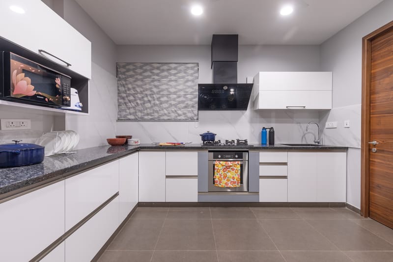 L-shaped kitchen with white handleless cabinets, granite worktop, built-in oven and marble backsplash, Hyderabad