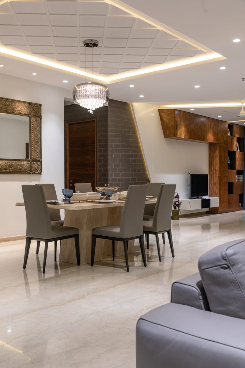 Dining area with marble-top table, grey upholstered chairs, crystal chandelier and coffered cove-lit ceiling, Hyderabad