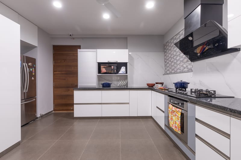White modular kitchen with granite counters, black chimney, stainless steel fridge and built-in oven, Hyderabad