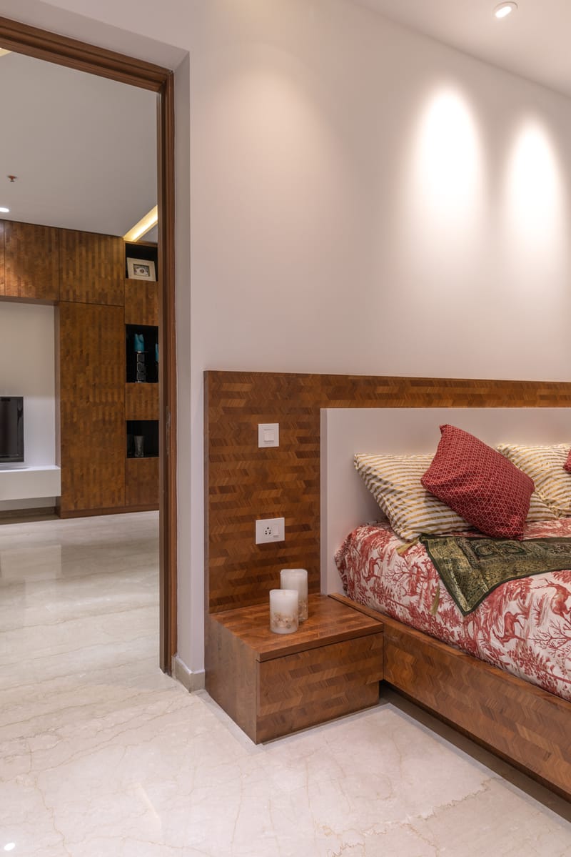 Bedroom corner with wooden brick-pattern headboard, floating bedside, candles and red toile bedding, Hyderabad