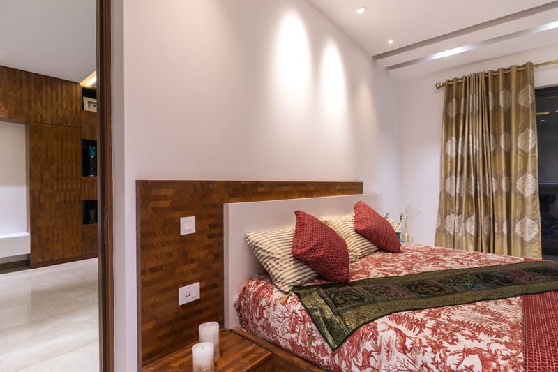 Master bedroom with parquet wood headboard, gold floral drapes and red bolster cushions, Hyderabad home