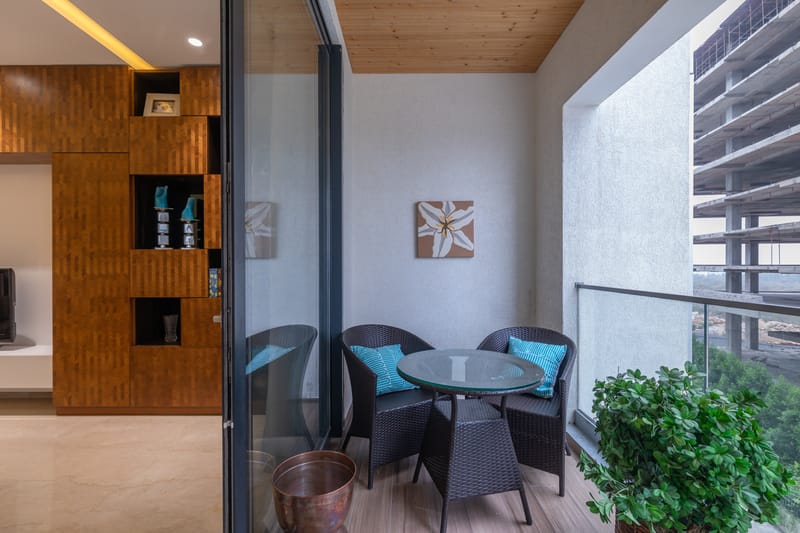 Balcony with wicker bistro set, teal cushions, flower wall art and wood-grain flooring, Hyderabad high-rise
