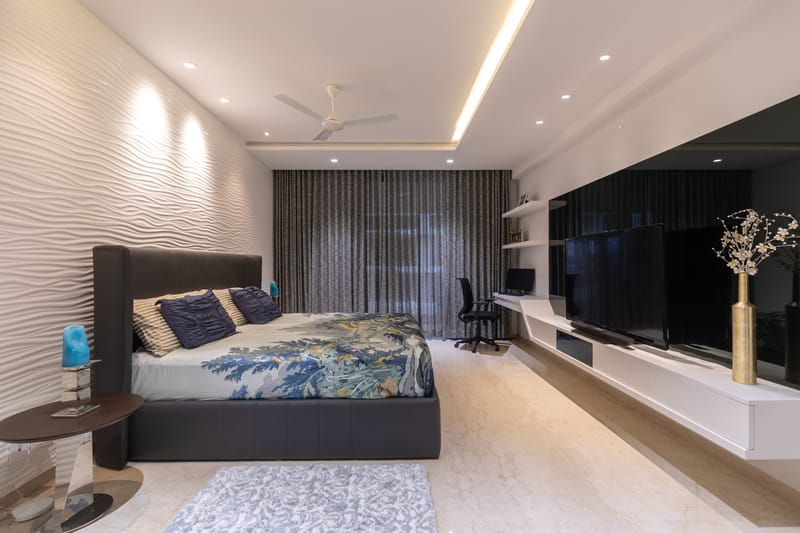 Master bedroom with rippled white accent wall, upholstered bed, sheer drapes and wide floating TV unit, Hyderabad