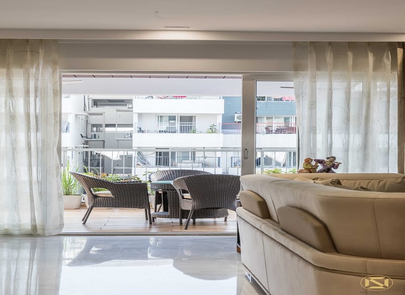 Living room view through sheer curtains onto a wicker-seated balcony overlooking apartment blocks, Hyderabad
